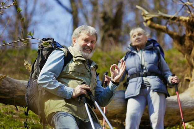 Fühlen Sie sich richtig und Freude. Alter Familienpaar von Mann und Frau im Touristenoutfit, das an grünem Rasen nahe an Bäumen an sonnigem Tag geht. Konzept von Tourismus, gesundem Lebensstil, Entspannung und Zusammengehörigkeit.