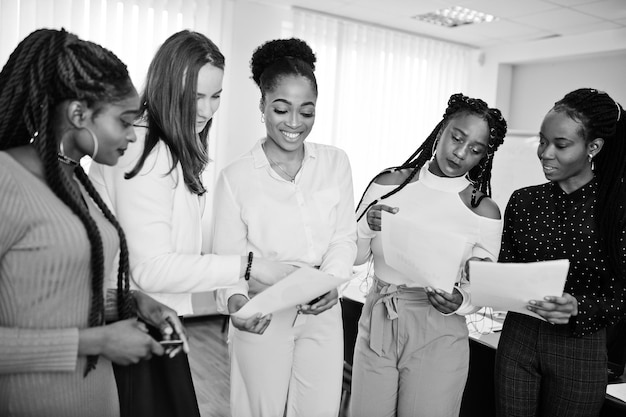 Fünf gemischtrassige Geschäftsfrauen, die im Büro mit Papieren an den Händen stehen Vielfältige Gruppe weiblicher Angestellter in formeller Kleidung