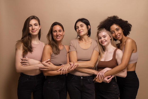 Fünf hübsche Frauen mit kaukasischem und afrikanischem Aussehen in nackter Kleidung verflechten ihre Hände auf beigem Hintergrund