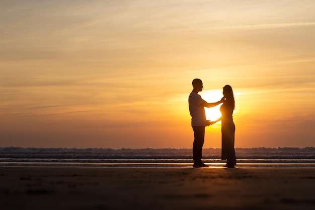 Fürsorgliche Familie, die bei Sonnenuntergang am Strand spazieren geht. Mann und Frau in Freizeitkleidung, die in der Abenddämmerung am Wasser spazieren. Liebe, Familie, Naturkonzept