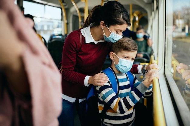 Fürsorgliche Mutter und Sohn mit schützenden Gesichtsmasken, die mit dem öffentlichen Bus reisen