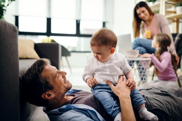 Fürsorglicher Vater verbringt Zeit mit seinem kleinen Sohn zu Hause Mutter und Tochter kommunizieren im Hintergrund