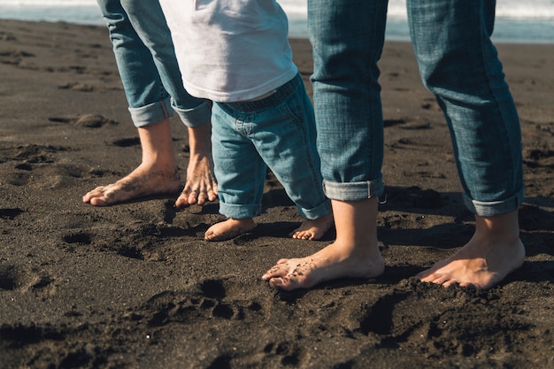 Füße des Babys und der Eltern, die auf sandige Küstenlinie gehen