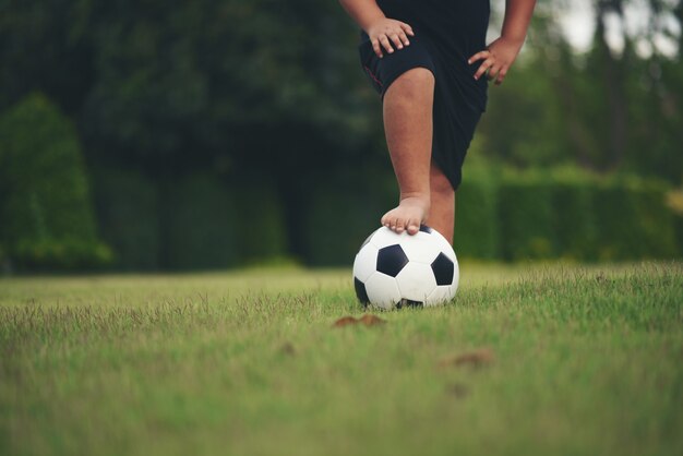 Füße des kleinen Jungen, die Fußball an der Rasenfläche halten