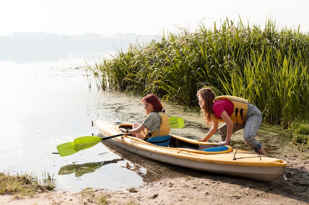 Full Shot Frauen bekommen Kajak aus dem Wasser