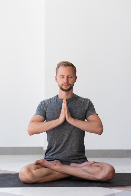 Full Shot Mann macht Sukhasana Pose innen auf Matte