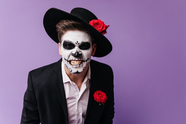 Furchterregender Kerl im Zombie-Outfit, der Wut ausdrückt. Studiofoto des Mannes im Muertos-Kostüm, das während der Halloween-Party herumalbert.