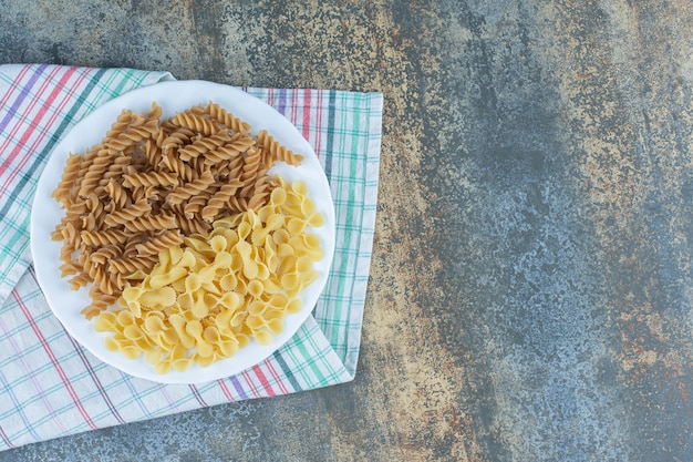 Kostenloses Foto fusilli-nudeln und farfalle-nudeln in der schüssel auf dem handtuch auf der marmoroberfläche anbraten.