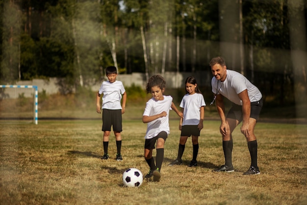 Kostenloses Foto fußballspielende kinder unter aufsicht eines fußballtrainers