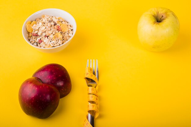 Gabel in Maßband zwischen Obst und Schüssel Müsli