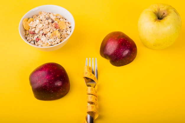 Gabel in Maßband zwischen Äpfeln und Schüssel Müsli