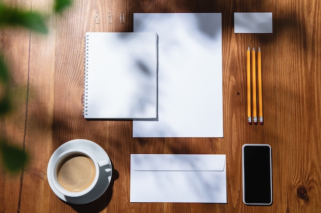 Gadgets, Kaffee, Arbeitsgeräte auf einem Holztisch im Innenbereich. Kreativer, gemütlicher Arbeitsplatz im Home Office, inspirierendes Modell mit Pflanzenschatten auf der Oberfläche. Konzept des Remote-Büros, freiberuflich, Atmosphäre.