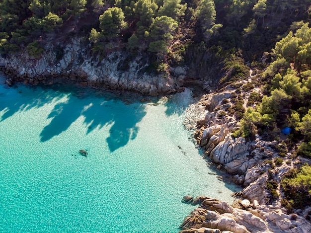 Ägäische Seeküste mit blauem transparentem Wasser, Grün herum, Felsen, Büsche und Bäume, Blick von der Drohne, Griechenland