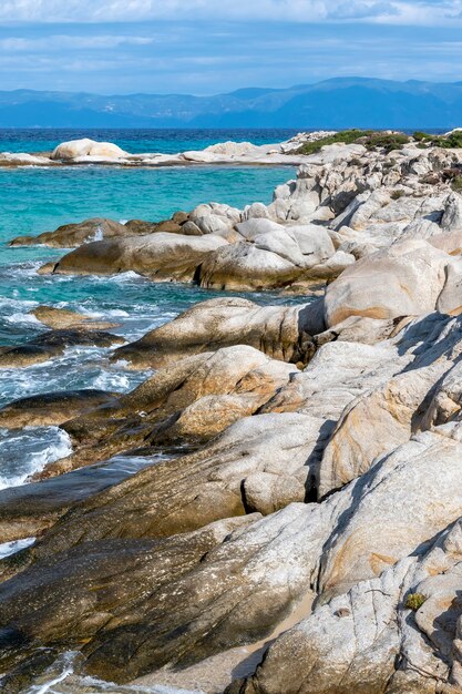 Ägäische Seeküste mit Felsen, Büschen und Land, blaues Wasser mit Wellen, Griechenland