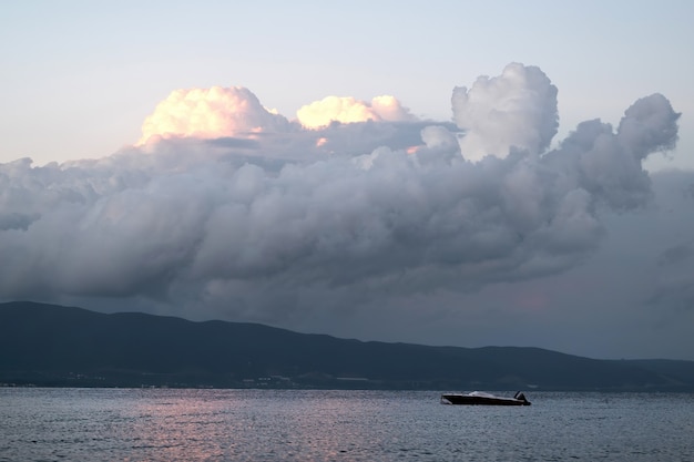 Ägäisches Meer mit einem Boot, üppige Wolken beleuchtet durch das Überstellen, Griechenland