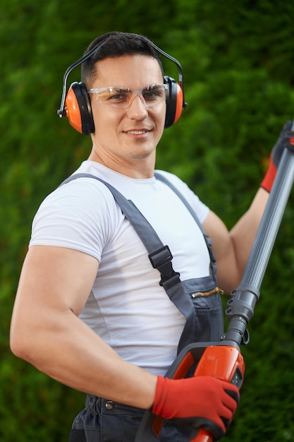 Gärtner steht in der Nähe einer Hecke mit elektrischem Trimmer in den Händen