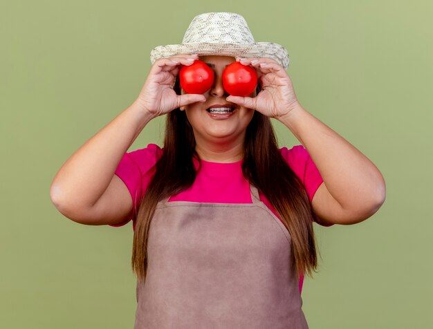 Gärtnerin mittleren Alters in der Schürze und im Hut, die frische Tomaten halten