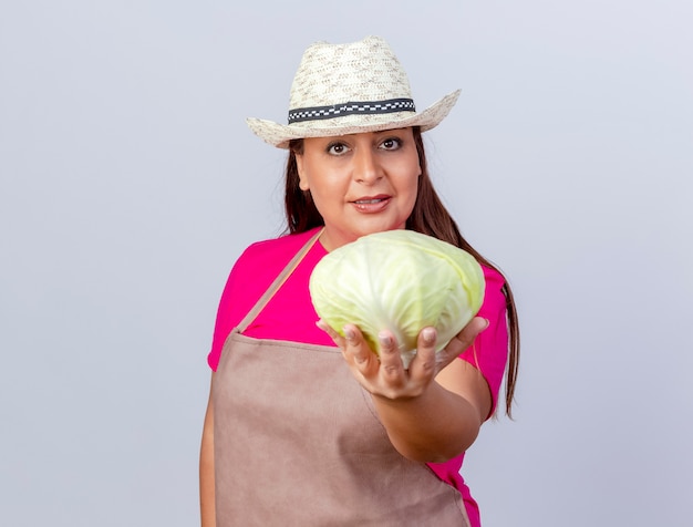 Gärtnerin mittleren Alters in Schürze und Hut, die Kohl mit einem selbstbewussten Lächeln zeigt