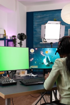 Gamer-frau, die online-videospiele während der gaming-meisterschaft spielt und sich den green-screen-chroma-key-computer mit isoliertem display anschaut. streaming-weltraum-shooter-spiel für junge spieler mit joystick
