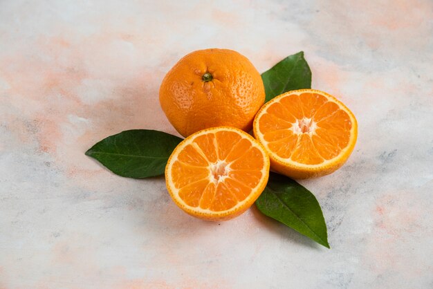 Ganz und halb geschnittene Clementinenmandarinen mit Blättern über bunter Oberfläche