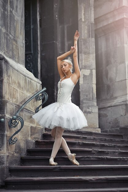 Ganzaufnahme einer schönen jungen Balletttänzerin, die anmutig auf der Treppe eines alten Gebäudes in der Stadt posiert.