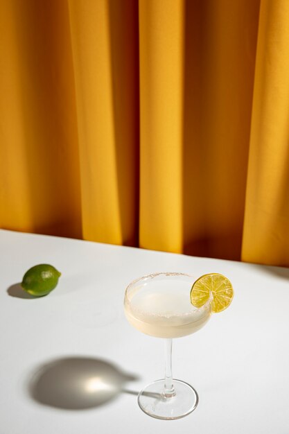 Ganze Limette mit Margarita-Cocktail in einem Untertassenglas auf dem Tisch in der Nähe des Vorhangs