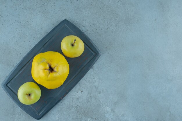 Ganze Äpfel und Quitten auf einem Brett, auf dem Marmorhintergrund. Foto in hoher Qualität
