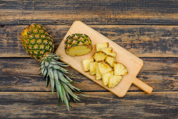 Ganze und geschnittene Ananas in einer Schneidebrett-Draufsicht auf einer Holzschmutzfläche