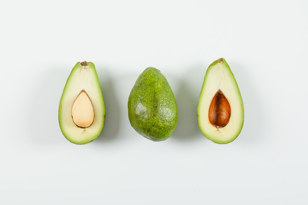 Ganze und geschnittene Avocado auf weißer Oberfläche. Draufsicht.