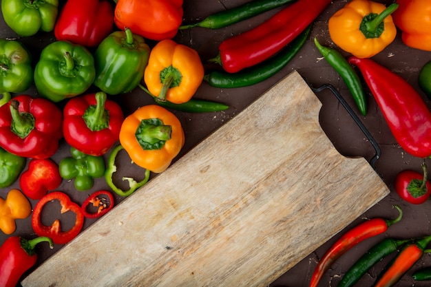 ganze und geschnittene Paprika mit Schneidebrett auf kastanienbraunem Tisch