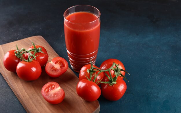 Ganze und geschnittene Tomaten und ein Glas Tomatensaft auf dem blauen Hintergrund.