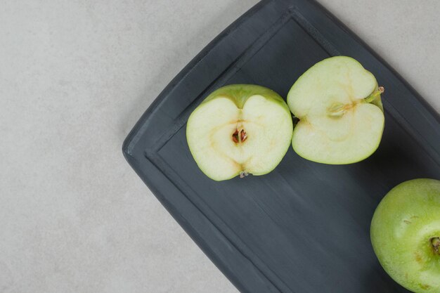 Ganze und halbe grüne Äpfel auf dunklem Teller schneiden