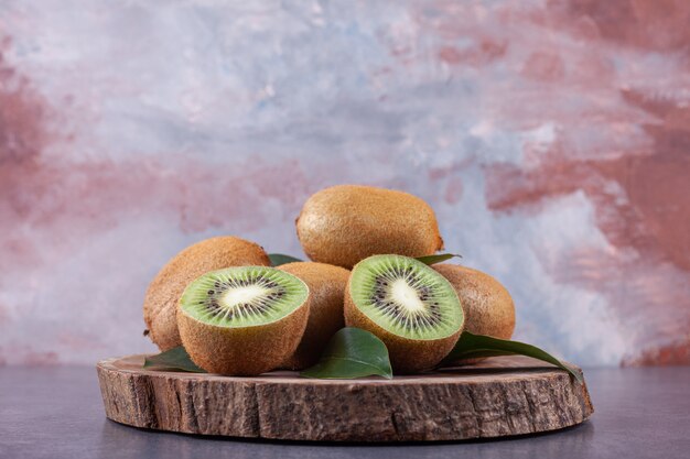 Ganze und in Scheiben geschnittene köstliche Kiwi mit Blättern auf einem Holzstück.