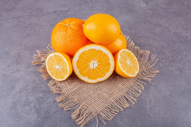 Ganze und in Scheiben geschnittene Orangenfrüchte mit frischen Zitronen auf einer Sackleinenoberfläche.