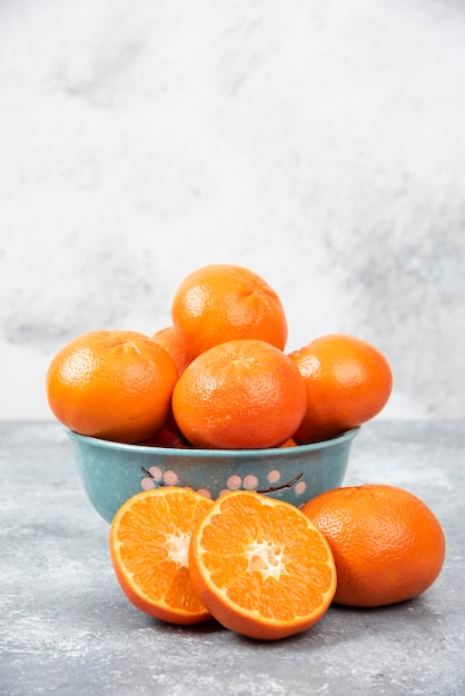 Ganze und in Scheiben geschnittene saftige frische Orangenfrüchte in eine Schüssel auf einem Steintisch stellen.