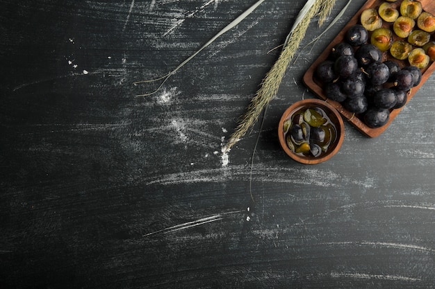 Ganze und in Scheiben geschnittene schwarze Pflaumen auf einem Holzbrett mit Kräutern beiseite