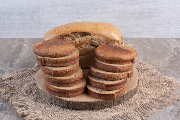 Ganzer Brotblock hinter Stapeln von geschnittenem Schwarzbrot auf einem Brett auf Marmorhintergrund. Foto in hoher Qualität