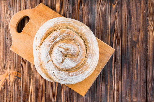 Ganzes rundes gebackenes Brot auf hackendem Brett über dem hölzernen Hintergrund