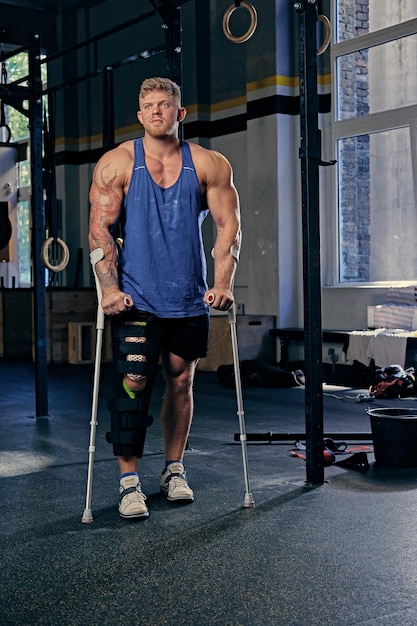 Ganzkörperbild eines riesigen Bodybuilders auf Krücken in einem Fitnessstudio.