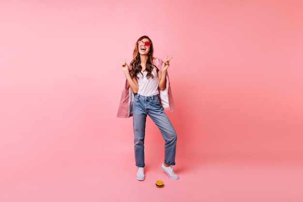 Ganzkörperporträt einer fröhlichen, stilvollen frau, die im studio tanzt rothaariges kaukasisches mädchen in trendigen jeans, das auf rosafarbenem hintergrund lächelt