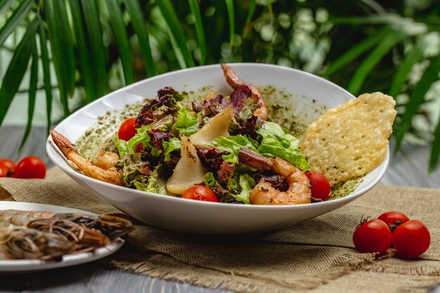 Garnelen-Caesar-Salat mit Kirschtomaten in einem weißen Teller auf einem Holztisch