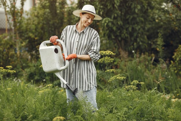 Gartenarbeit im Sommer. Frau, die Blumen mit einer Gießkanne wässert. Mädchen, das einen Hut trägt.