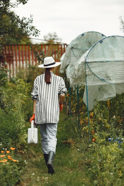 Gartenarbeit im Sommer. Frau, die Blumen mit einer Gießkanne wässert. Mädchen, das einen Hut trägt.