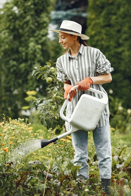 Gartenarbeit im Sommer. Frau, die Blumen mit einer Gießkanne wässert. Mädchen, das einen Hut trägt.