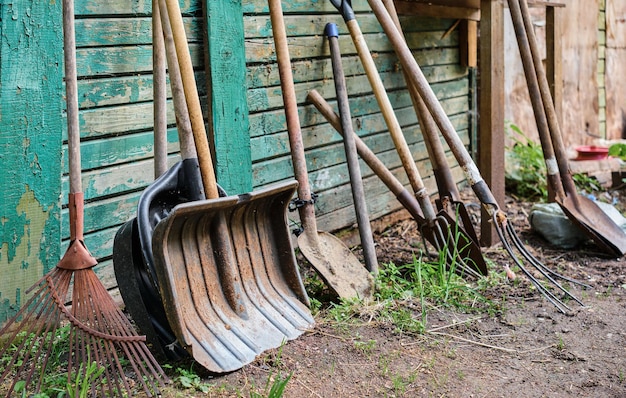 Gartenarbeit mit alten Werkzeugen an einer geschälten grünen Wand aus Holz Gemüsegarten und landwirtschaftliche Geräte Selektive Fokussierung von landwirtschaftlichen Handwerkzeugen auf dem Boden