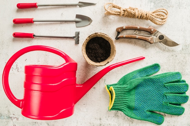 Kostenloses Foto gartengeräte; gießkanne; torftopf; gartenschere; seil und gartenhandschuhe auf konkreten hintergrund