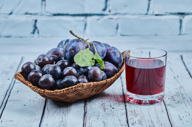 Gartenpflaumen in einem Korb auf einem blauen Hintergrund mit einem Glas Saft. Hochwertiges Foto