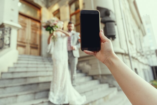 Gast, der Foto des kaukasischen romantischen jungen Paares macht, das Ehe in der Stadt feiert. Braut und Bräutigam. Familie, Beziehung, Liebeskonzept. Zeitgenössische Hochzeit