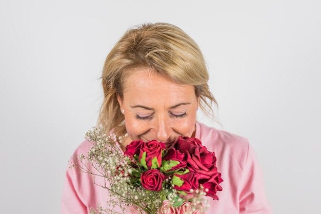 Kostenloses Foto gealterte frau in der rosafarbenen bluse, die schöne blüte riecht