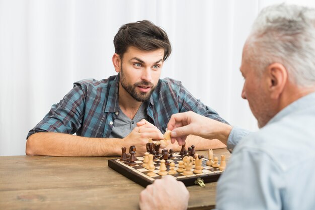 Gealterter Mann und junger Kerl, der bei Tisch Schach spielt